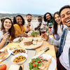 Group of friends enjoying a meal together outdoors with drinks and food.